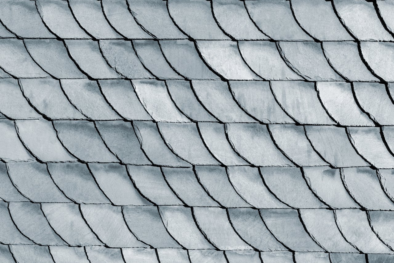 Overlapping pale gray slate roof shingles with dark seams and weathered surfaces.