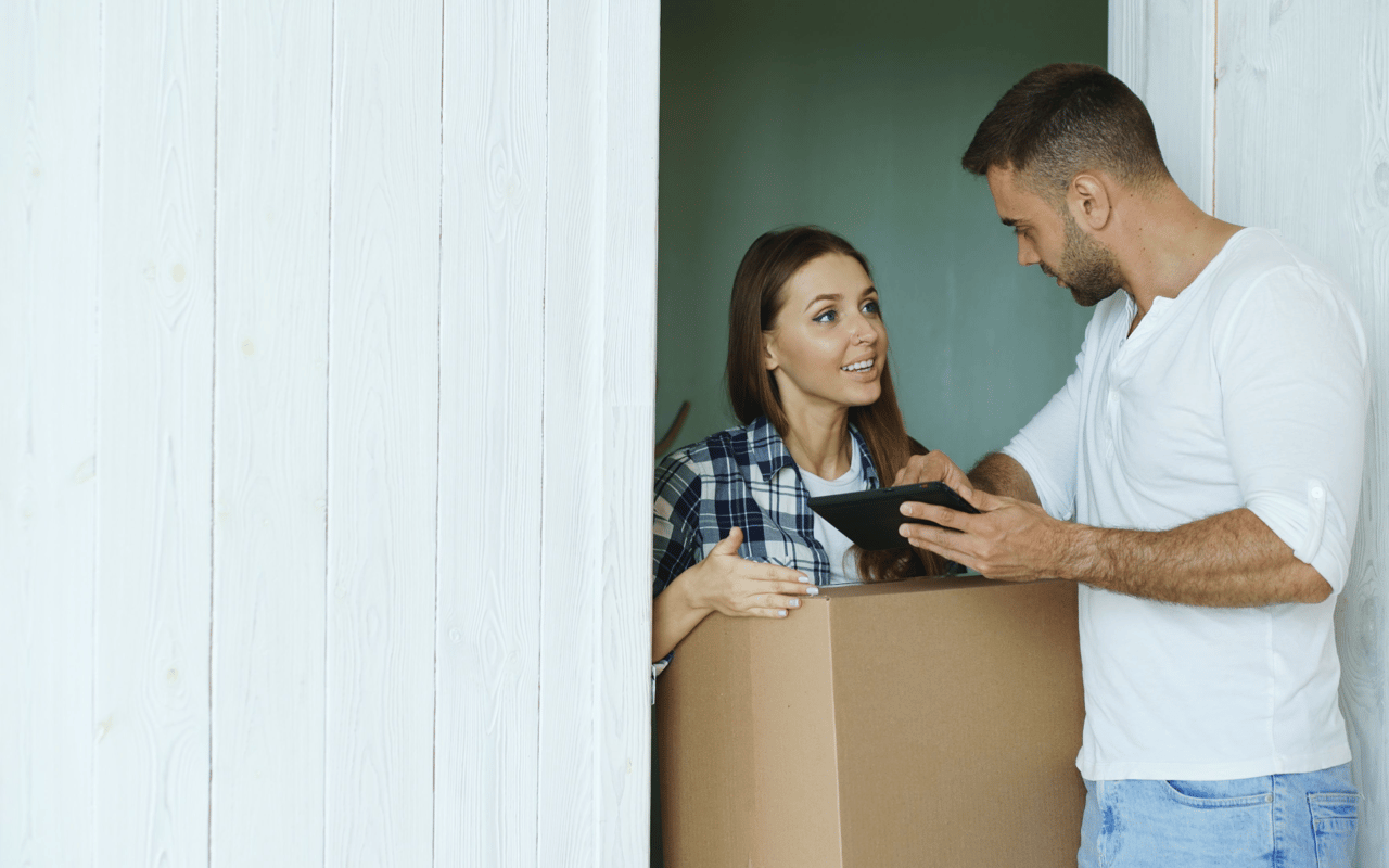 A couple discusses a tablet while moving boxes into their new home.