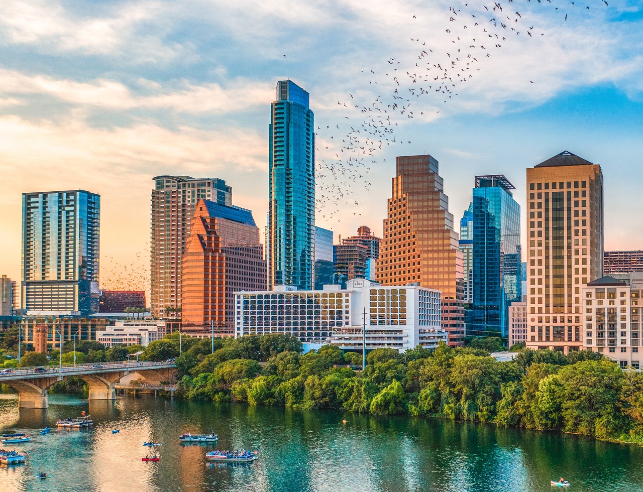 Austin skyline at golden hour above the Colorado River, with boats and bats.