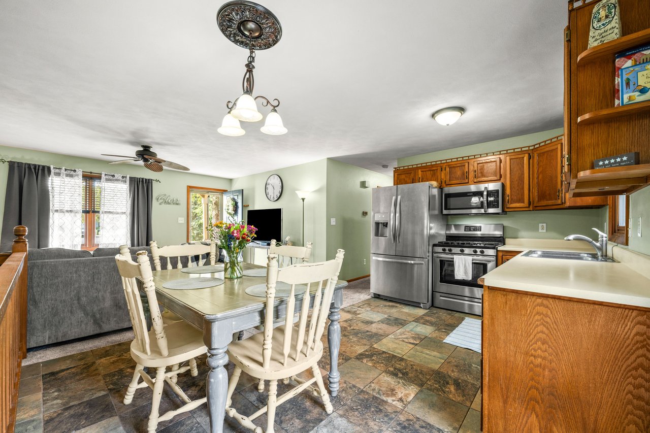 Open kitchen and dining area with wood cabinets, stainless appliances, and a pale table with white chairs.