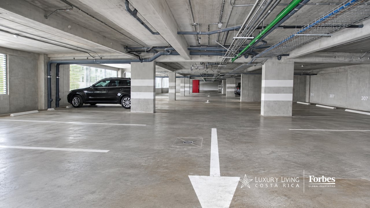 Underground parking garage with concrete pillars, a black car, and white directional arrows on the floor.