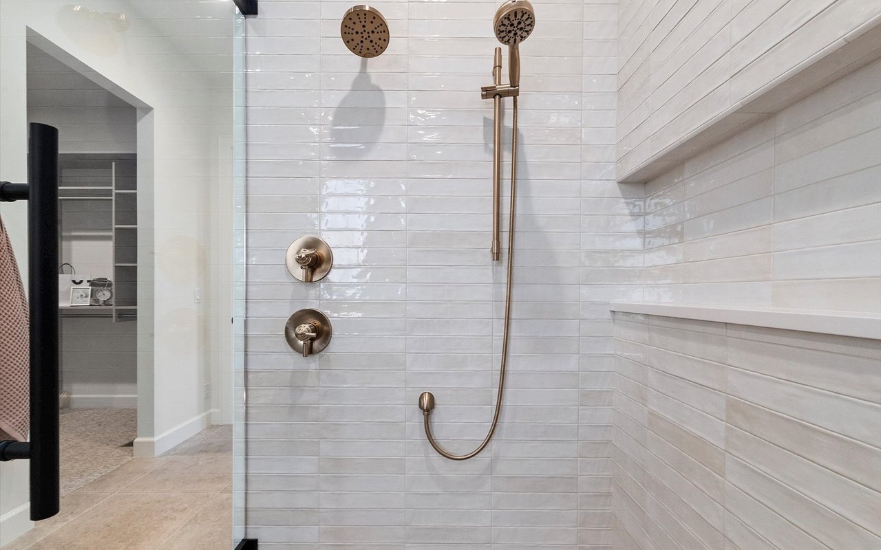 Close-up of the primary walk-in shower with pearly zellige tiles and brass hardware