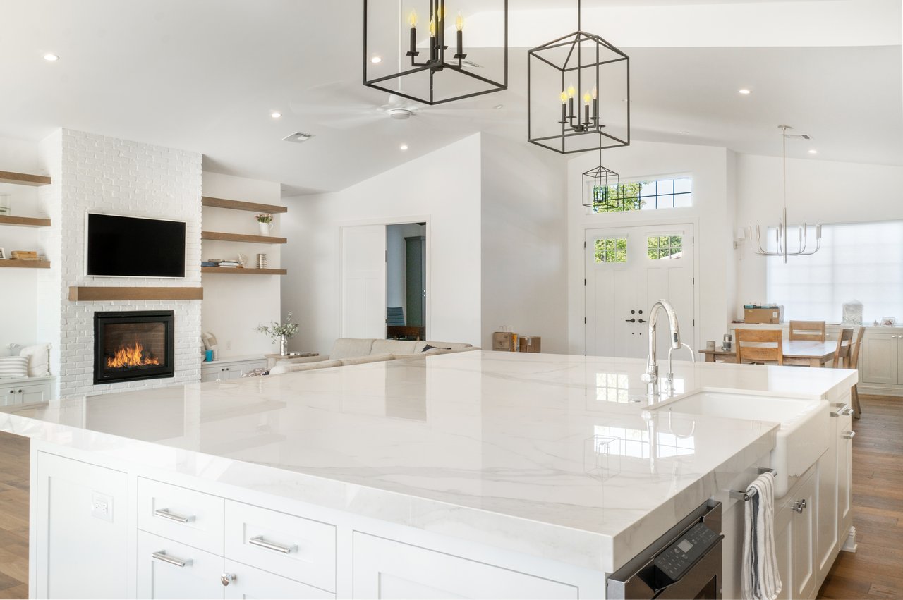 Open-plan kitchen with a large marble island and a white brick fireplace.