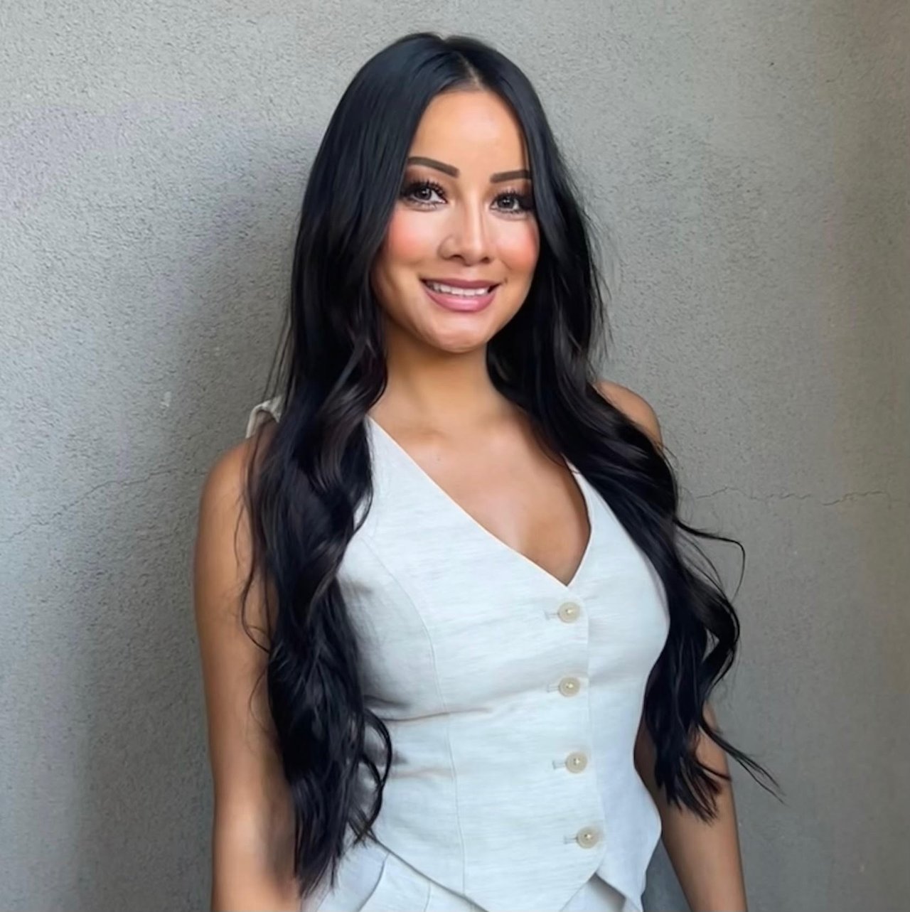 Gina Kwong in a white buttoned vest against a textured gray wall.