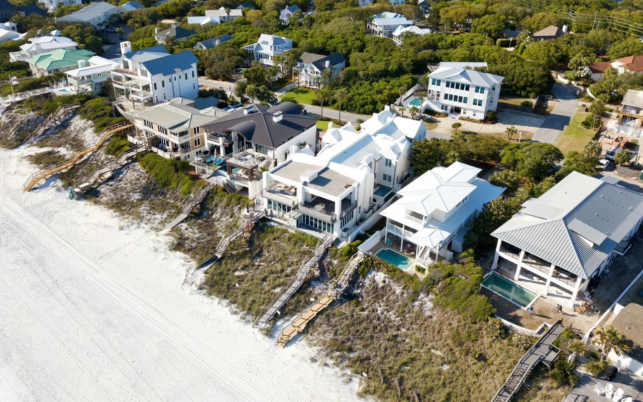 Aerial view of beachfront homes and sandy dunes along a coastal neighborhood.