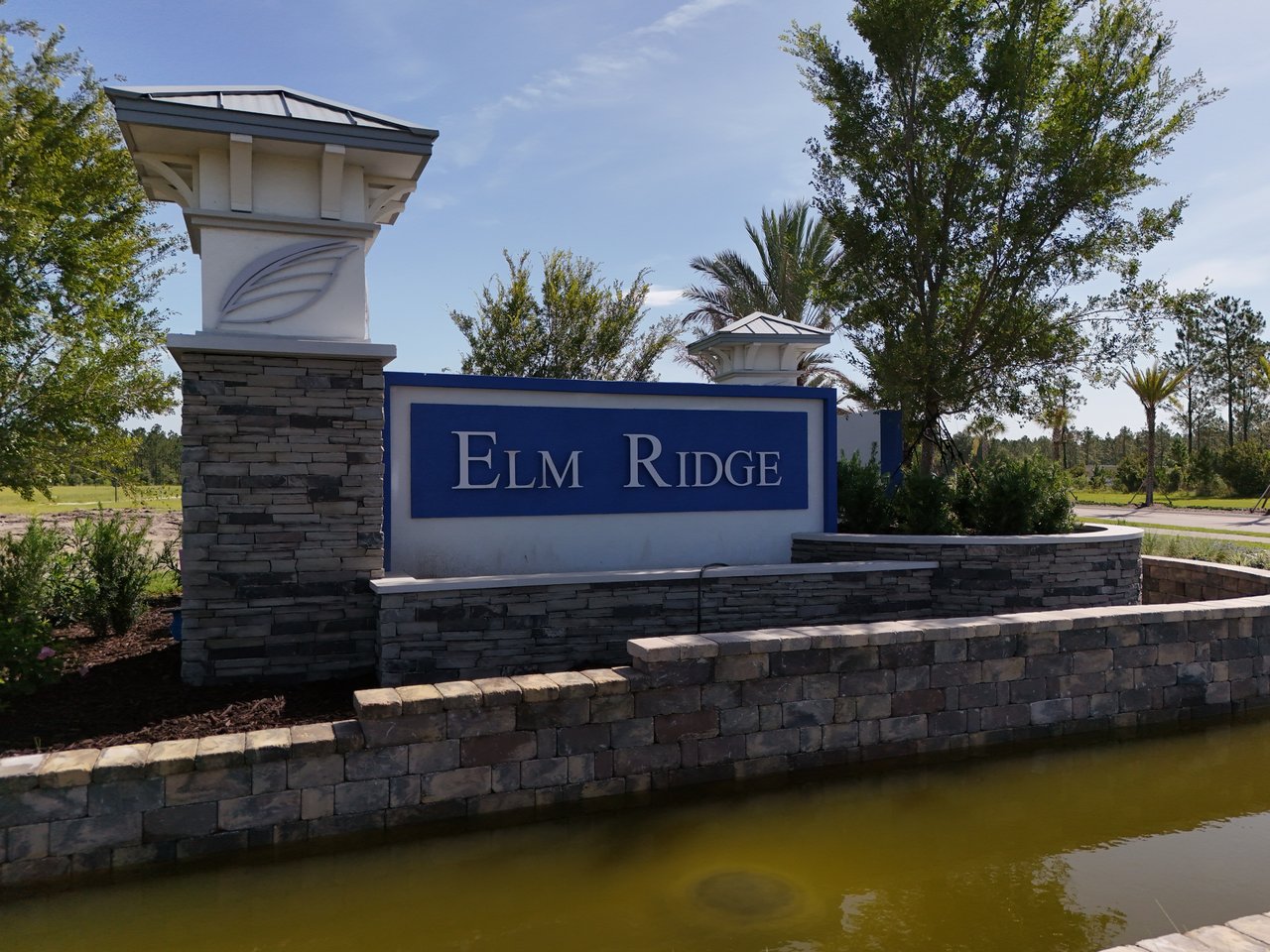 Elm Ridge entrance sign on a stone wall beside a pond.