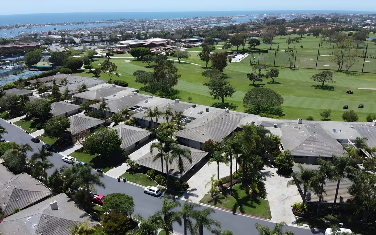 An aerial shot showing a residential neighborhood next to a lush golf course with a view of the ocean and bay.