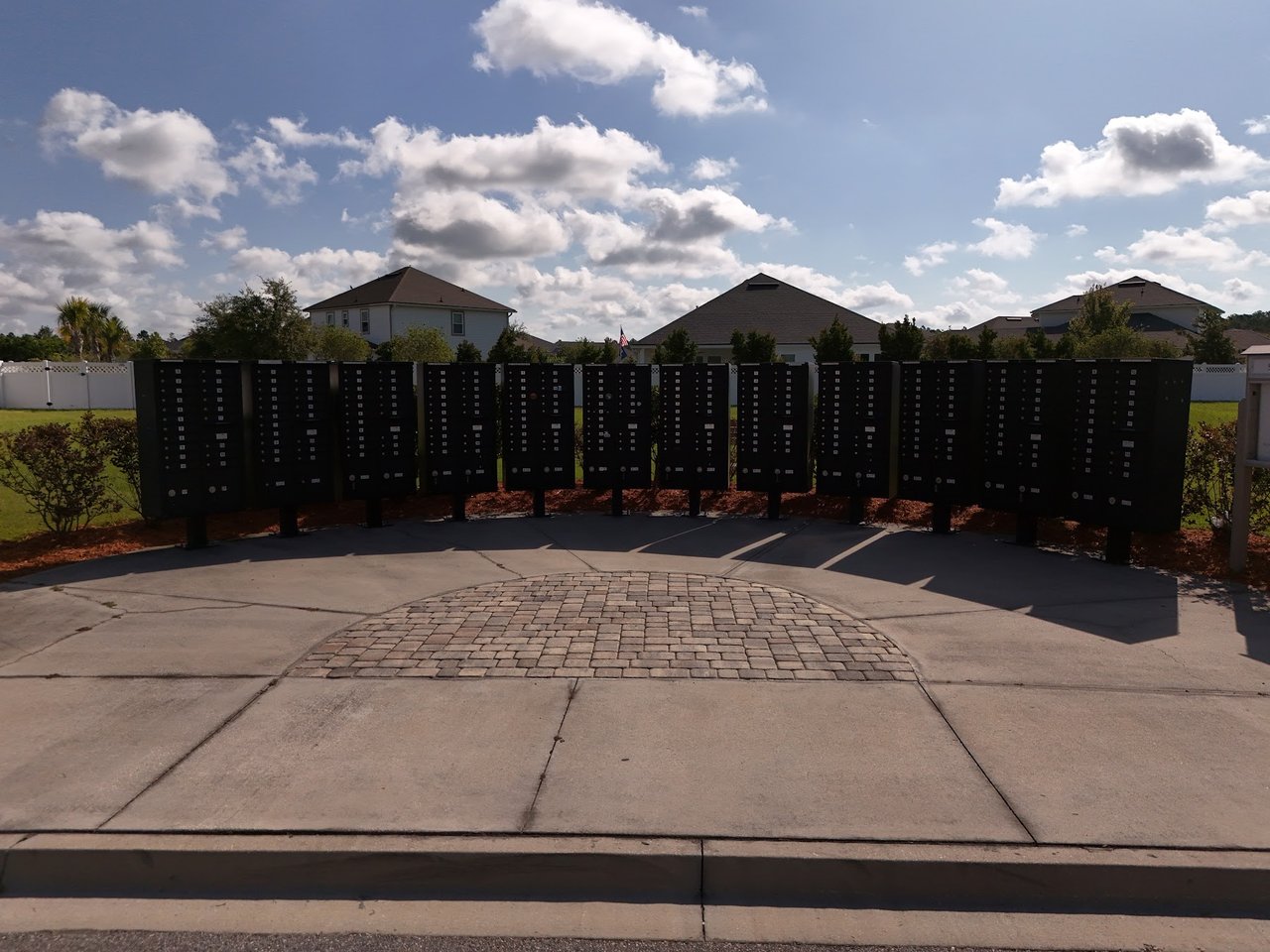 Community mailboxes along a paved driveway, with suburban homes behind them.