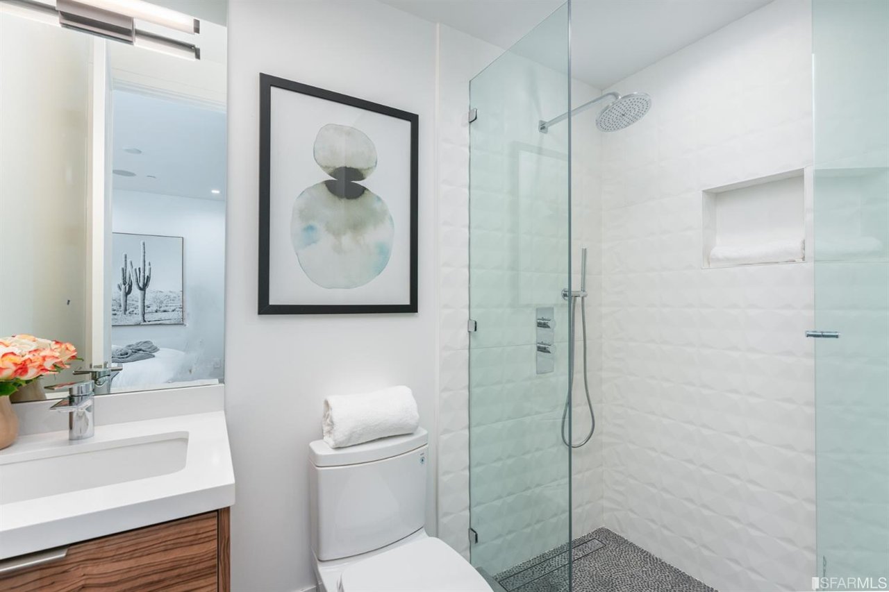 Modern bathroom with wood vanity, glass shower, and framed artwork