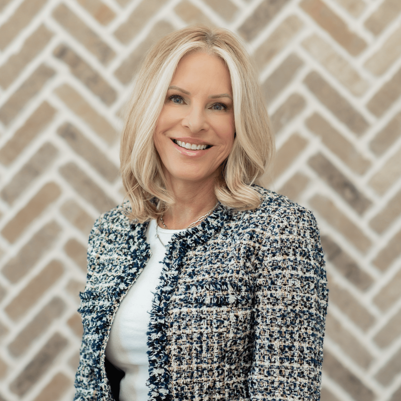 Tisa Stafford smiling in a textured navy and cream jacket against a geometric patterned wall.
