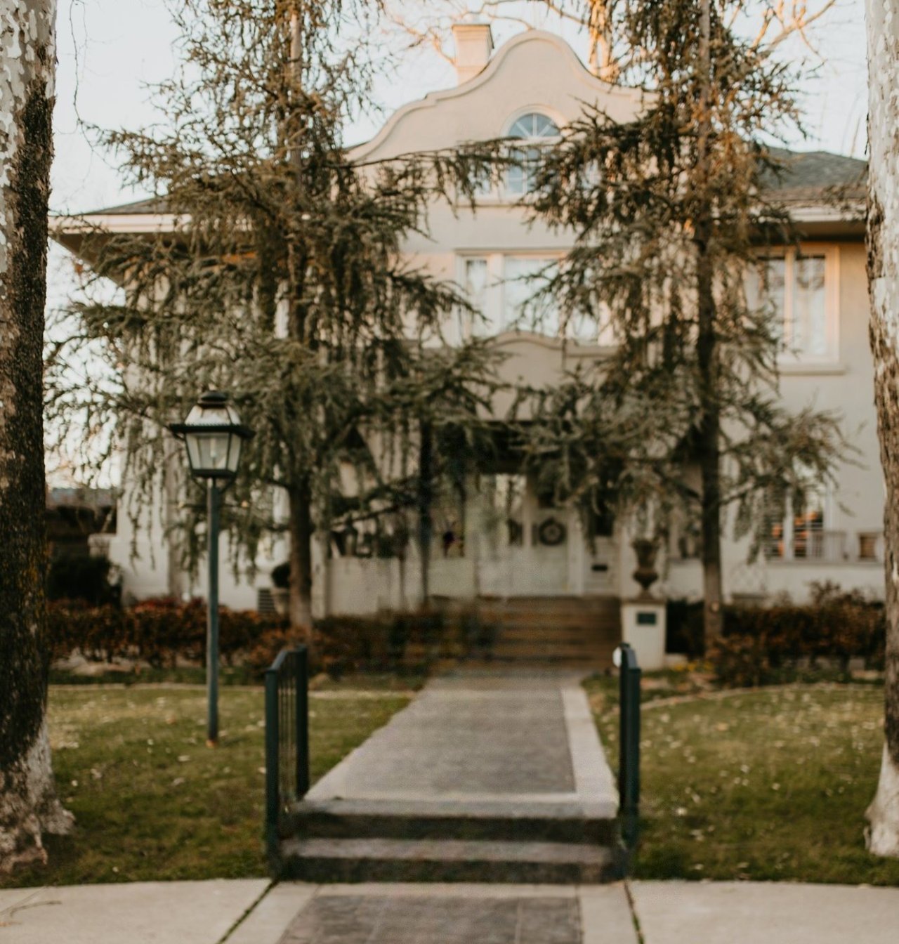 Large house with an arched facade, framed by bare trees and approached by a straight walkway.