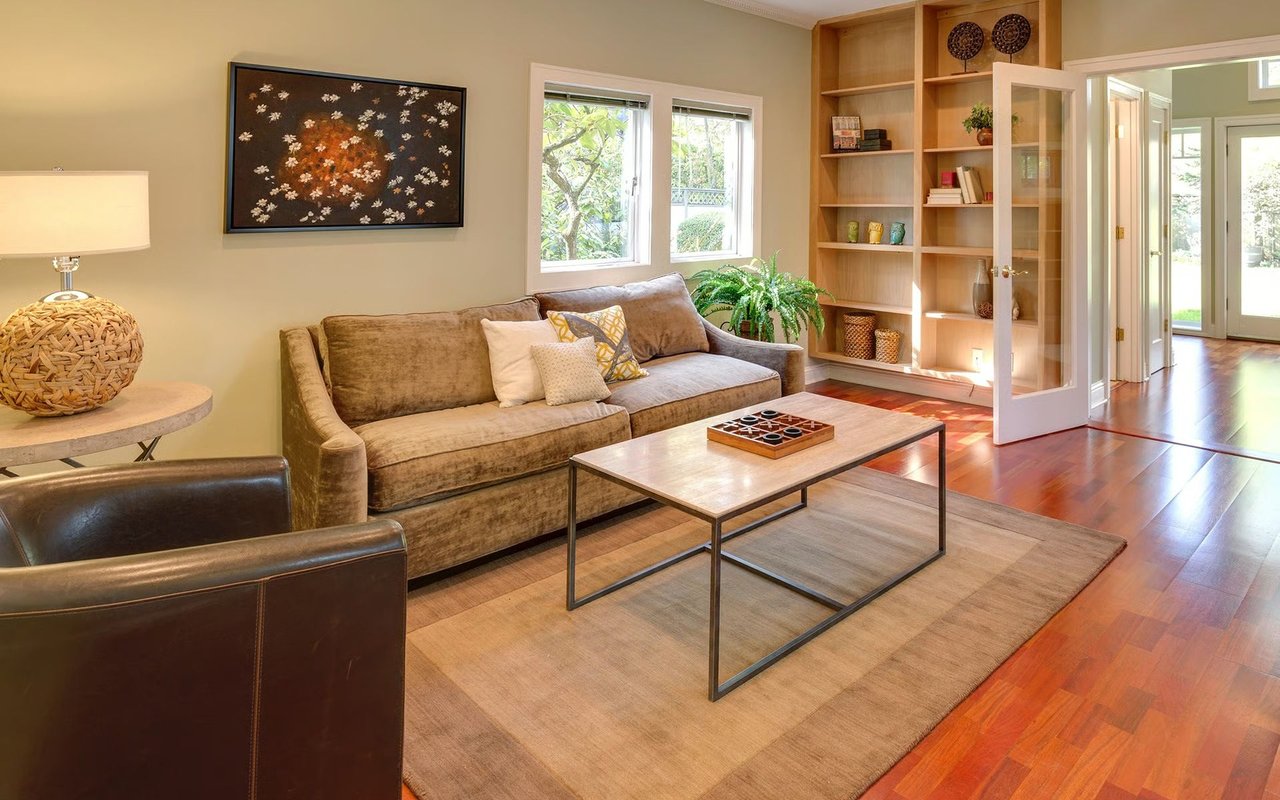 Furnished living room with built-in shelves, a brown sofa, and sunlit hardwood floors.