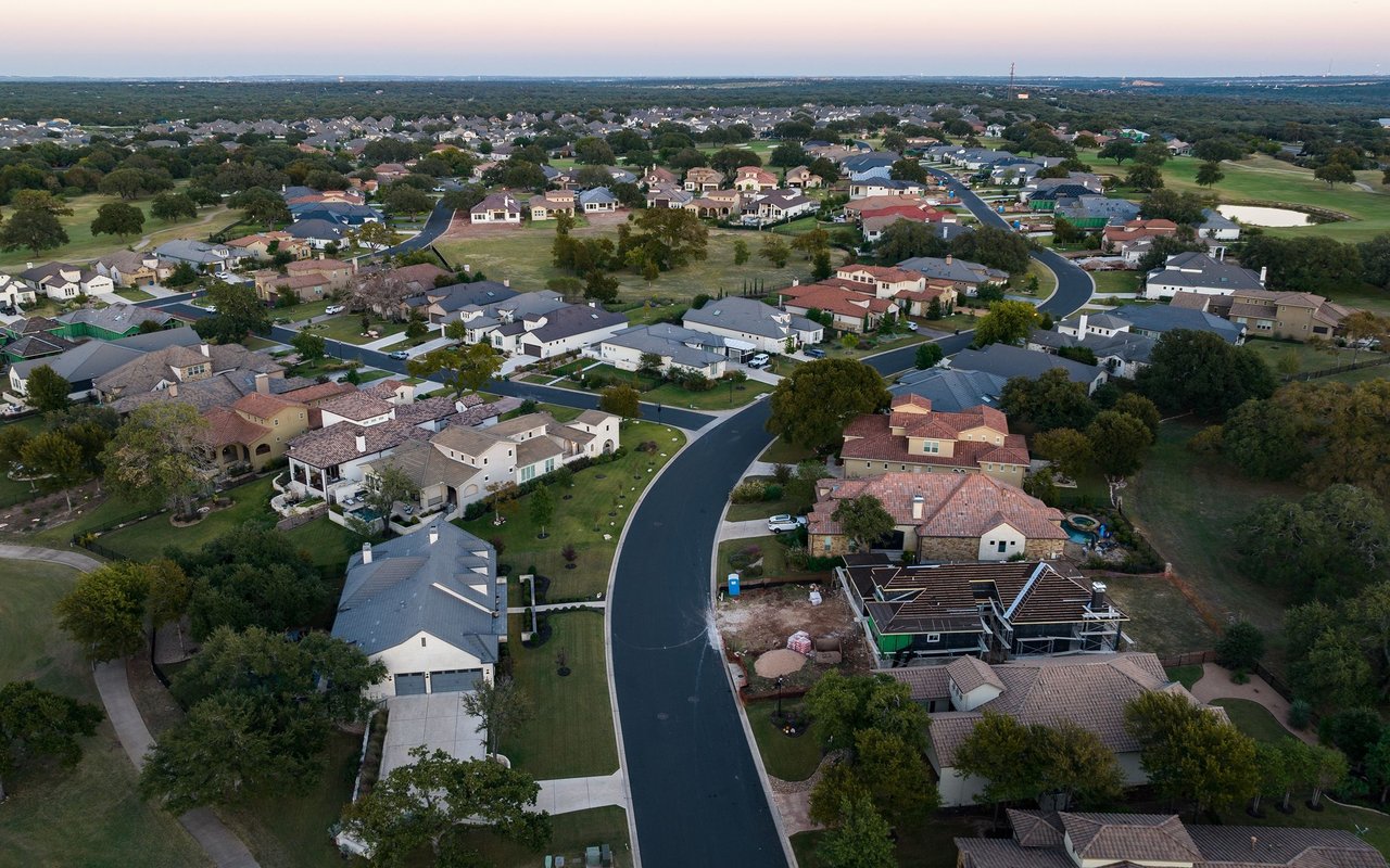 Aerial view of a residential neighborhood with a curving street and homes among mature trees.