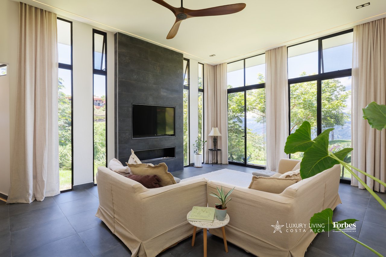 Contemporary living room with cream sofas, a dark stone fireplace wall, and floor-to-ceiling valley-view windows.