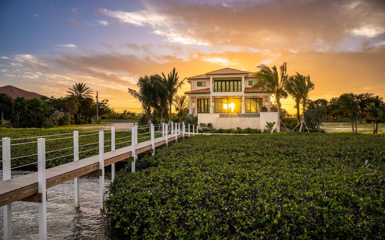 Waterfront home with a white-railed dock crossing mangroves at sunset.