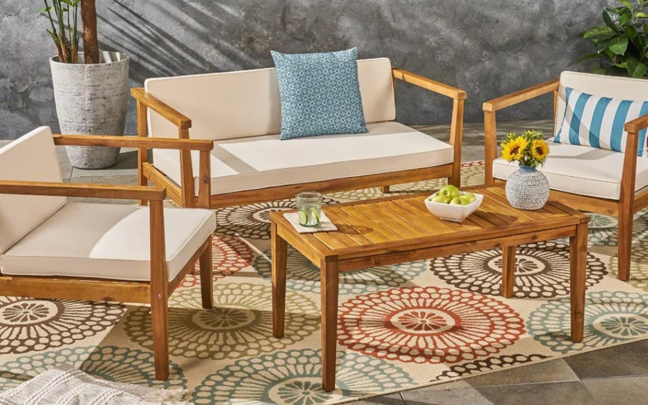 Outdoor patio seating with wood-framed cream sofas, a patterned rug, and a wooden coffee table.