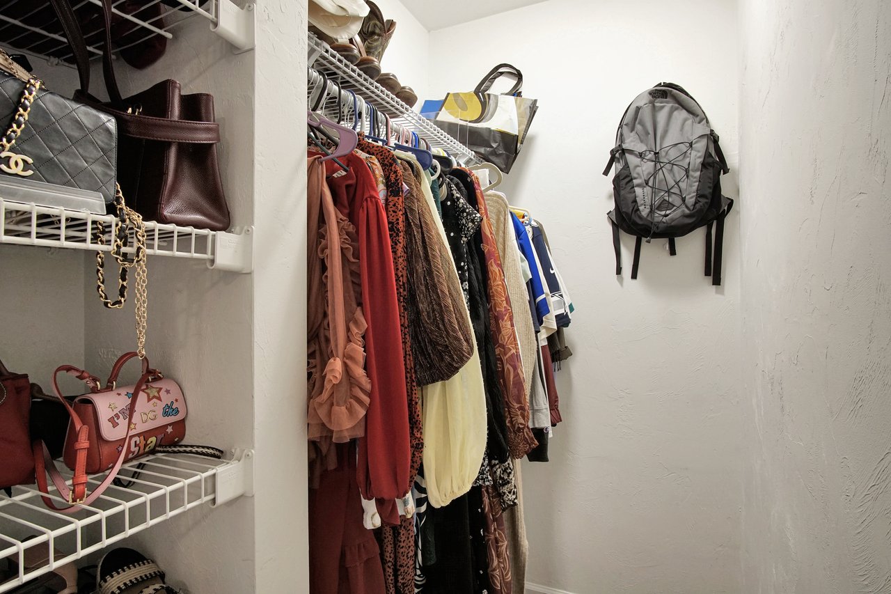 Closet with hanging dresses, various styles and colors, shelves holding handbags, and a gray backpack mounted on the wall, conveying organization.