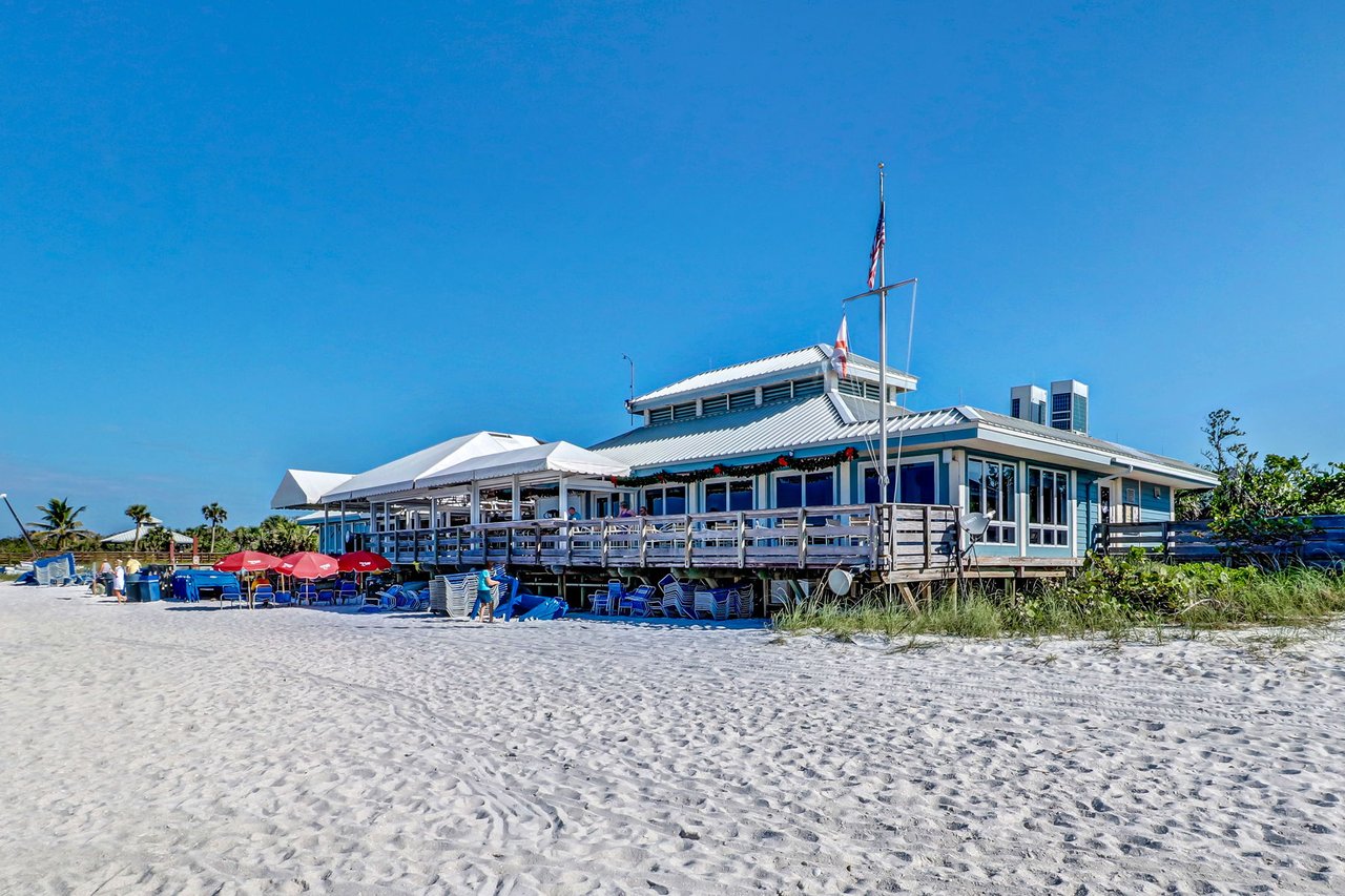 Beachfront clubhouse with a raised wooden deck and umbrellas on a sunny sandy beach.