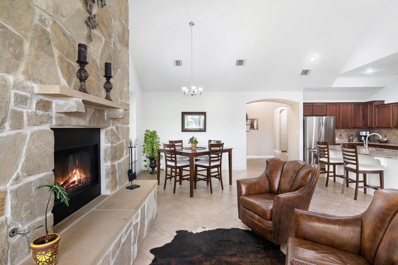Open-plan living and dining area with a stone fireplace, leather armchairs, and adjoining kitchen.