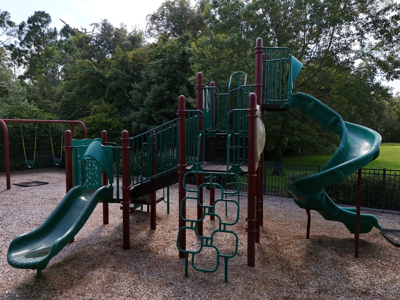 Neighborhood playground with teal slides and climbing equipment beneath mature trees.
