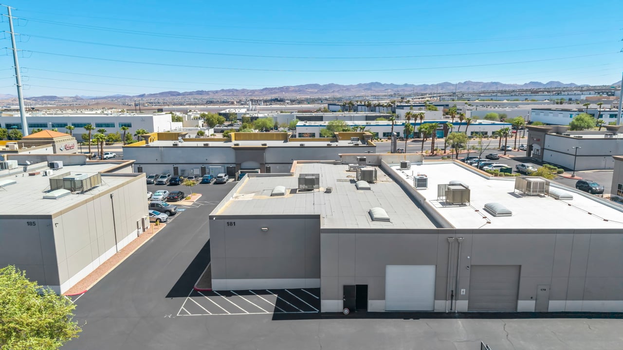 Commercial warehouse complex with flat rooftops, parking lanes, and mountains in the distance.