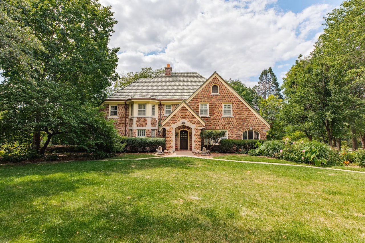 Two-story brick home with an arched entry, landscaped garden, and broad green lawn.