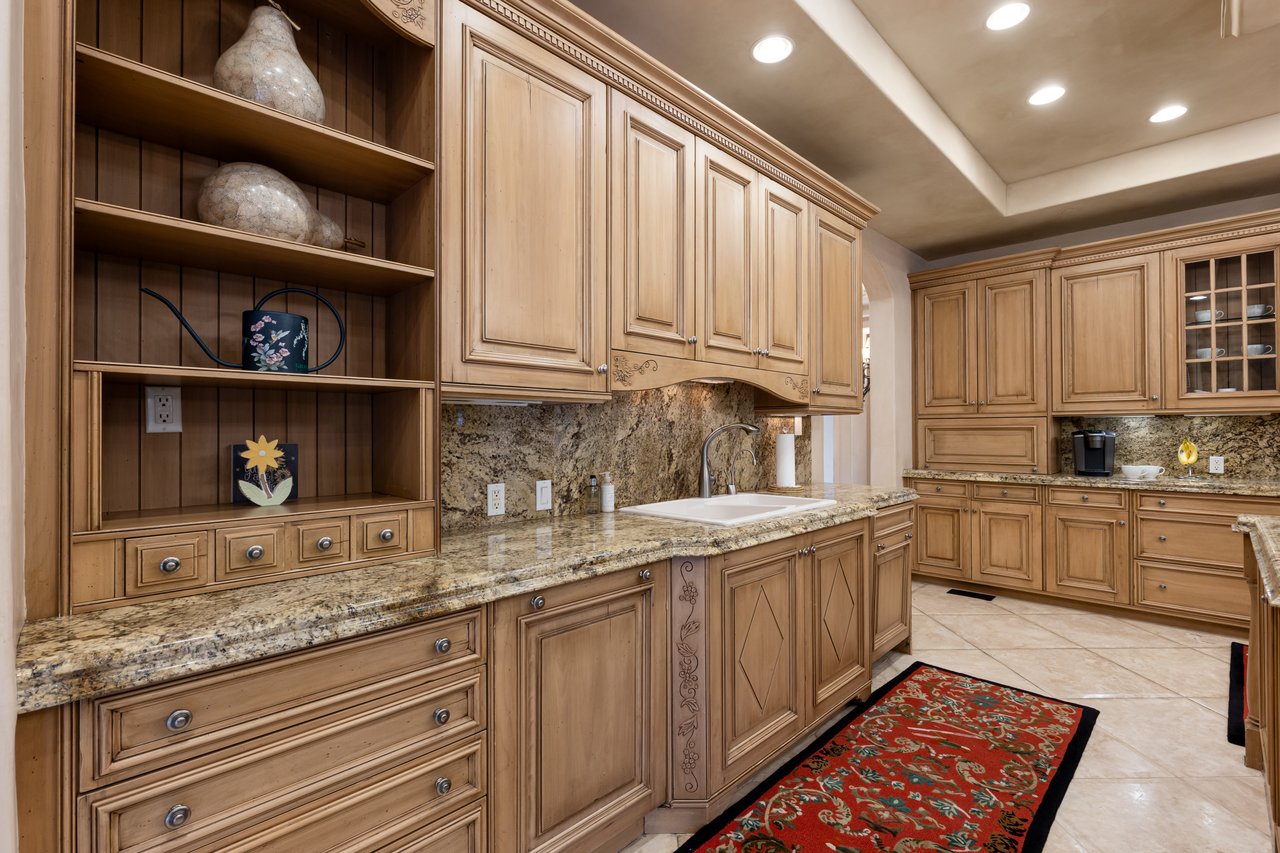 Kitchen with ornate wood cabinetry, granite counters, open display shelves, and a red patterned runner.