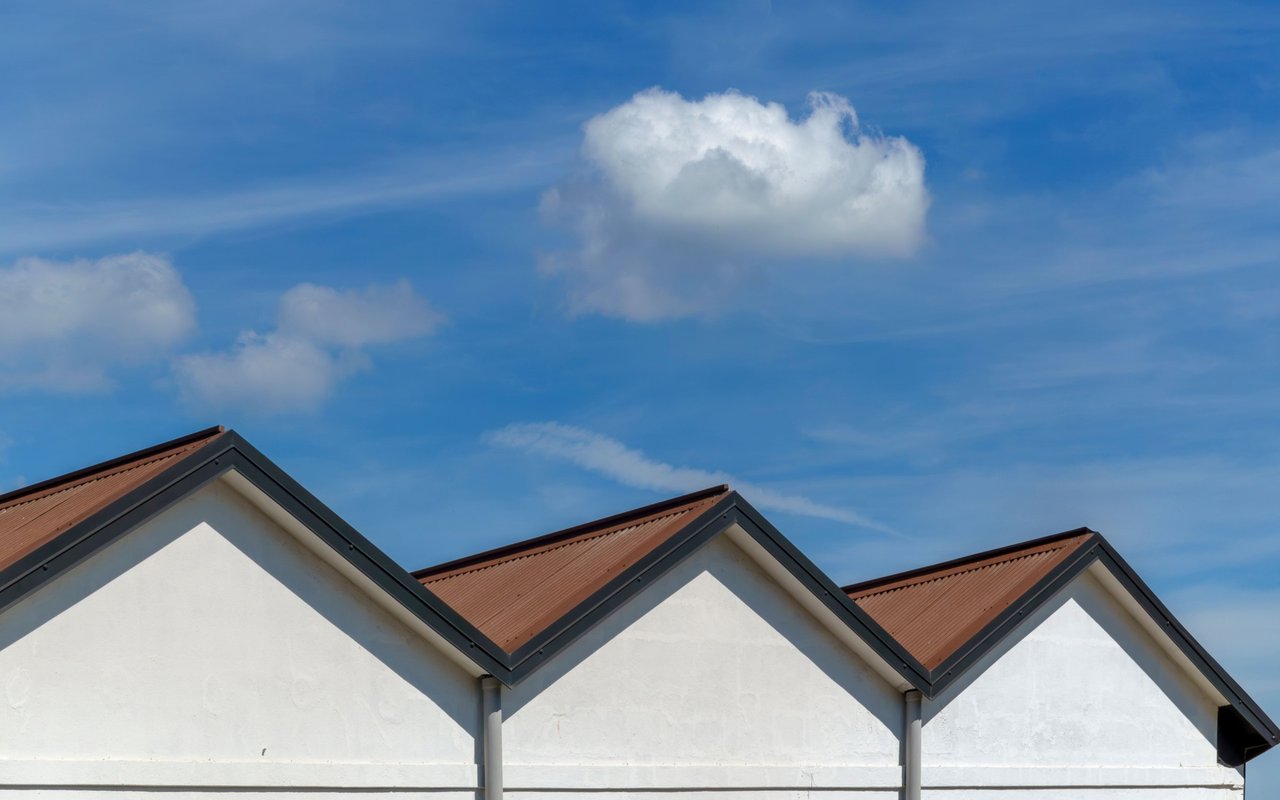 Repeating reddish-brown gabled roofs above white façades against a blue, cloud-dotted sky.