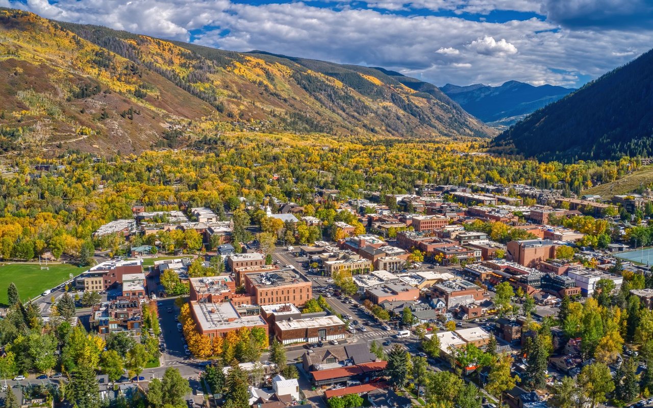 Aerial view of downtown Aspen amid golden autumn trees and mountain slopes.