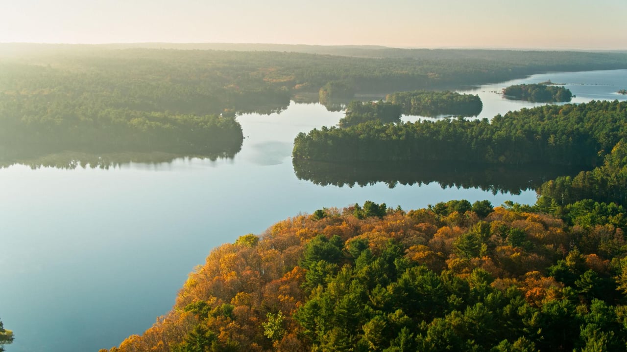 A lake winds among forested islands and shores with orange and gold autumn foliage.
