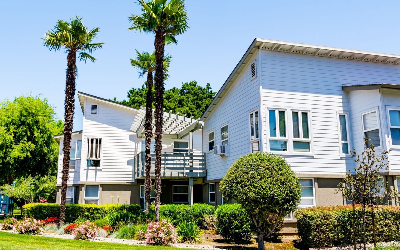 White multi-unit residence with balconies, palm trees, and colorful landscaping.