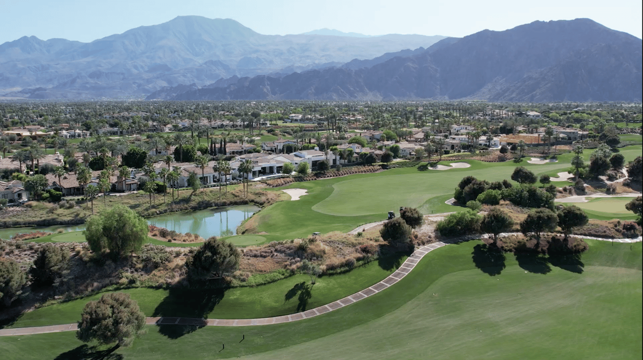 Aerial view of a La Quinta golf community with fairways, homes, water features, and mountains in the background
