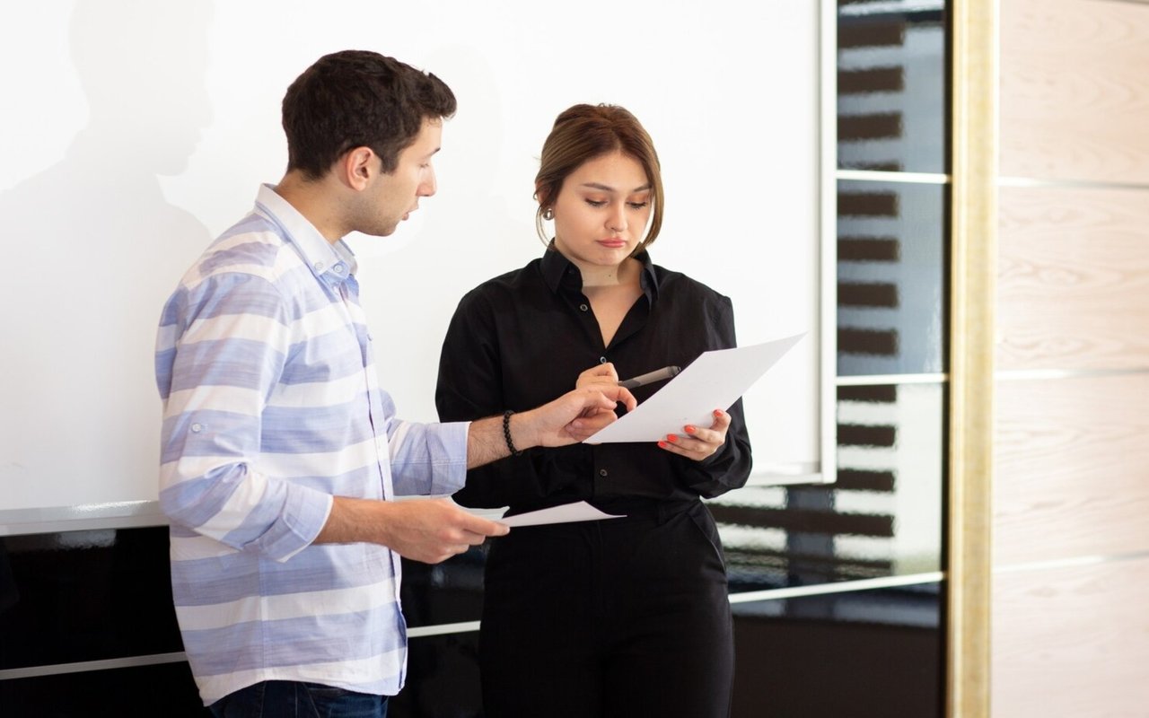 Two adults review paperwork together, with the man pointing to a page held by the woman.
