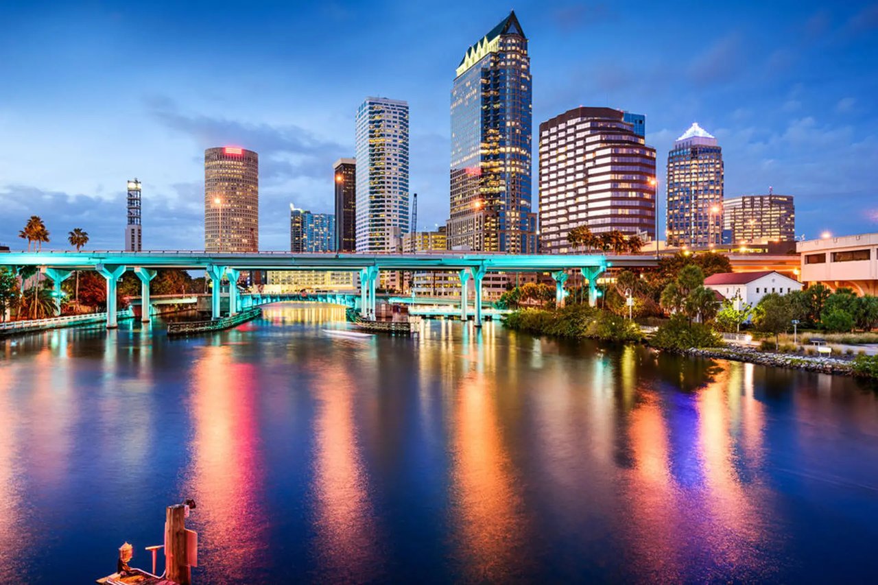 Downtown Tampa skyline and illuminated bridge reflected in the river at dusk.