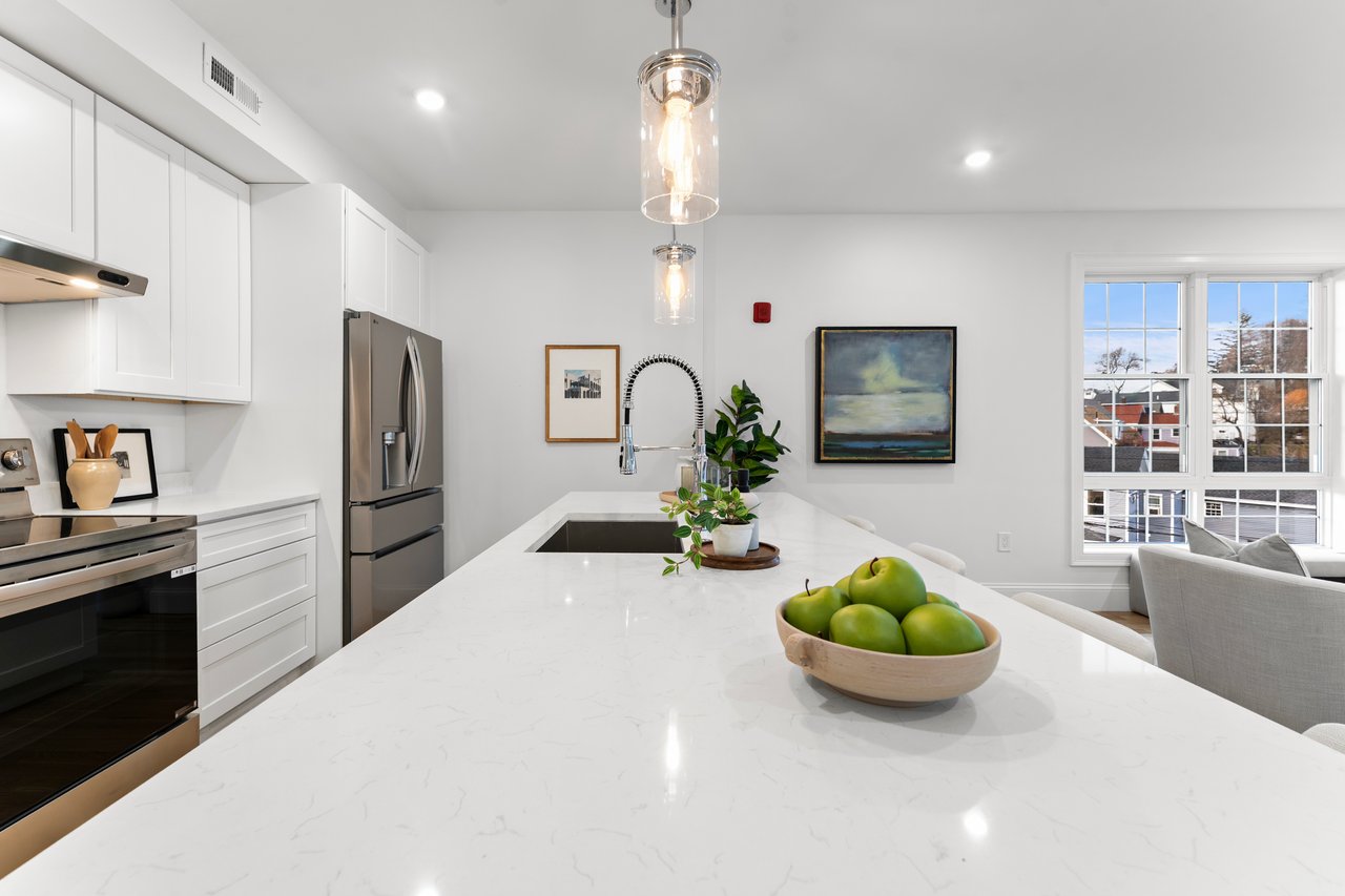 Bright kitchen with white cabinets, stainless steel appliances, and a quartz island topped with green apples.