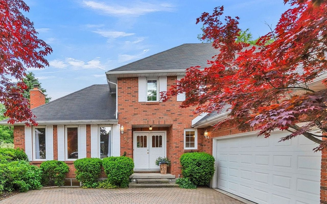 Red-brick two-story house with a double garage, paved driveway, and red autumn leaves.