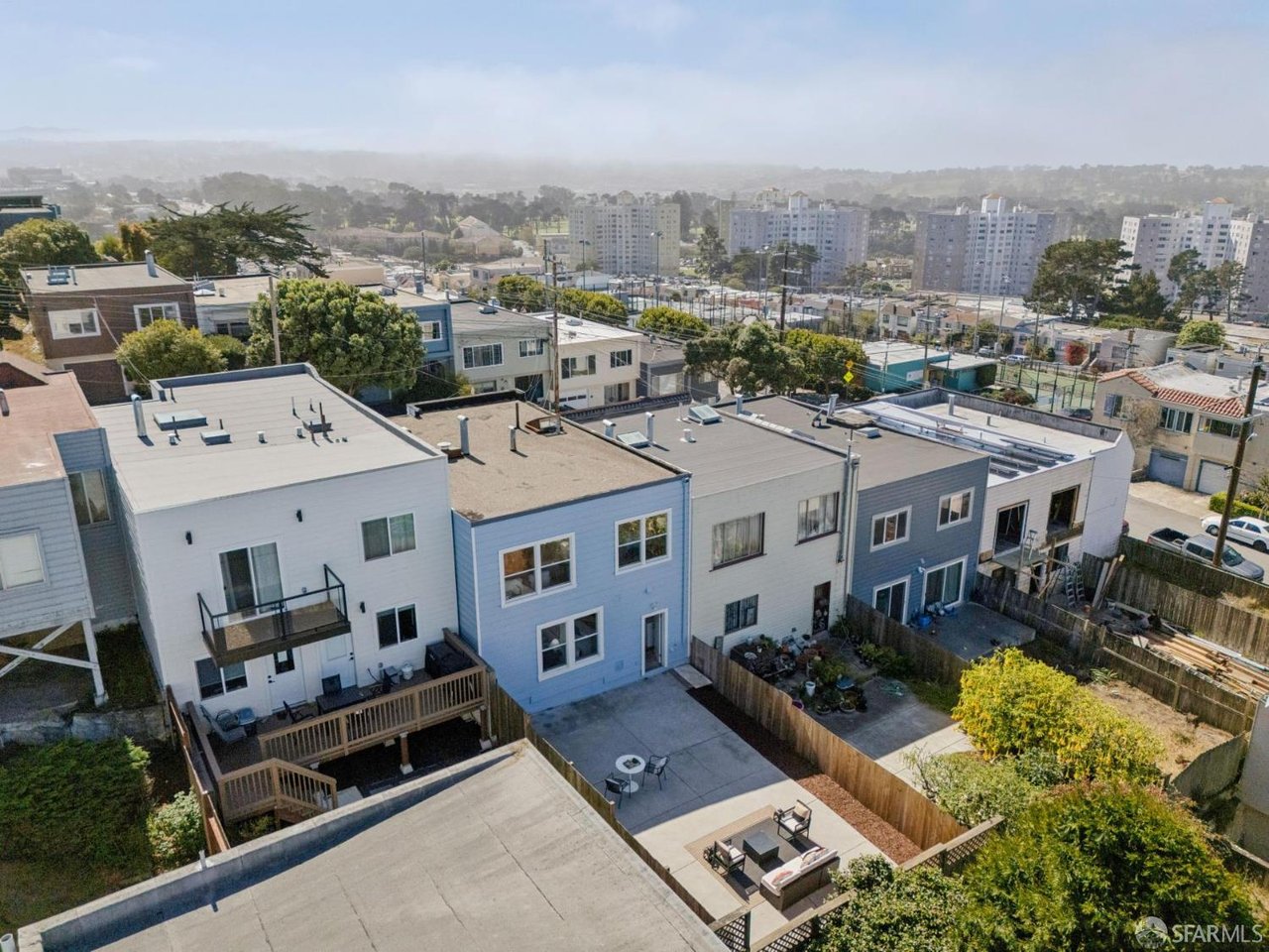 Aerial view of attached homes with fenced patios and distant apartment buildings.