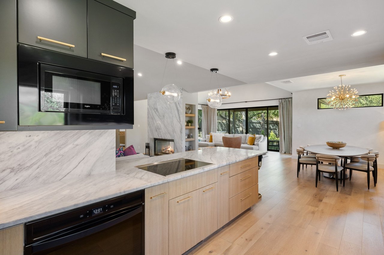 Open-plan kitchen with a marble island, pale wood cabinetry, and dining area beside the living room.