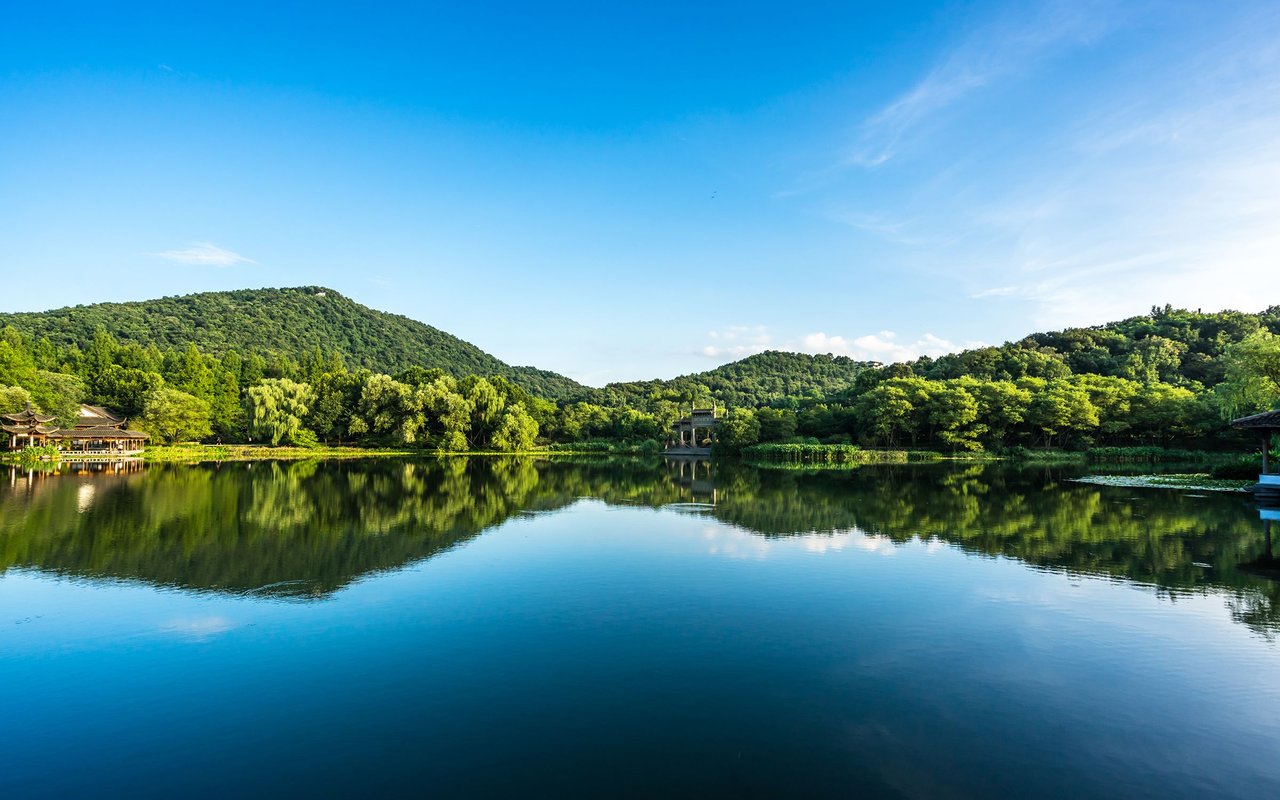 Still lake reflecting wooded hills, with a pavilion along the left shore.