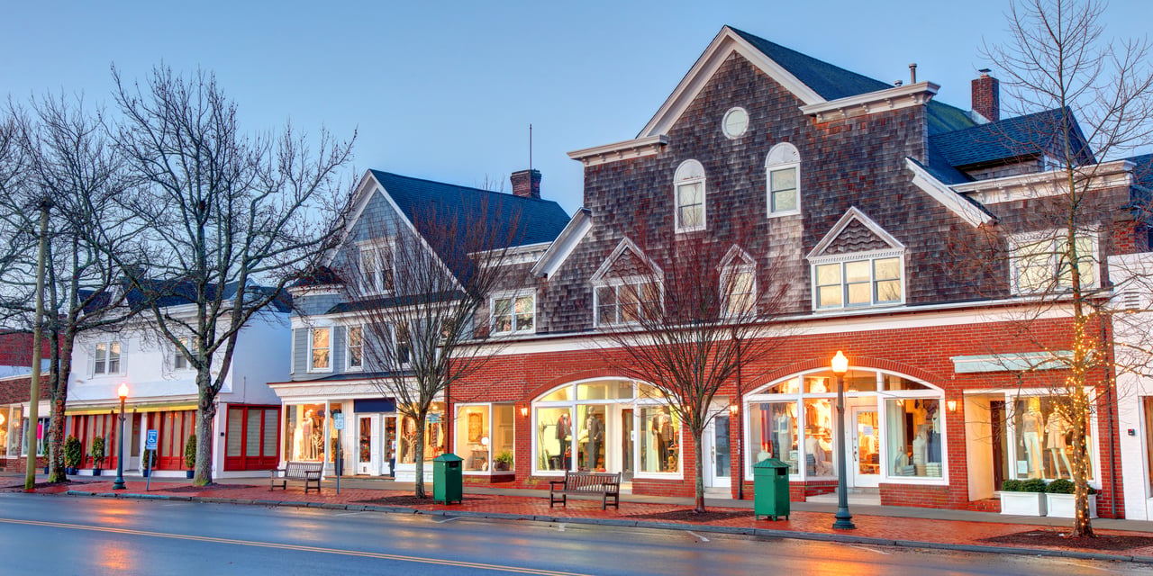 Village storefronts with red brick facades and shingled upper stories at dusk.