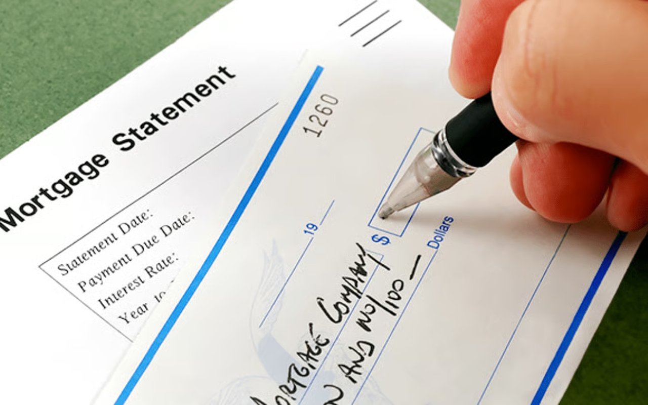A hand writes a mortgage payment check over a mortgage statement.