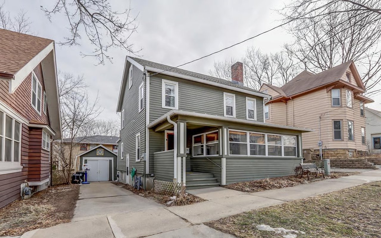 Gray two-story house with an enclosed front porch and driveway leading to a detached garage.