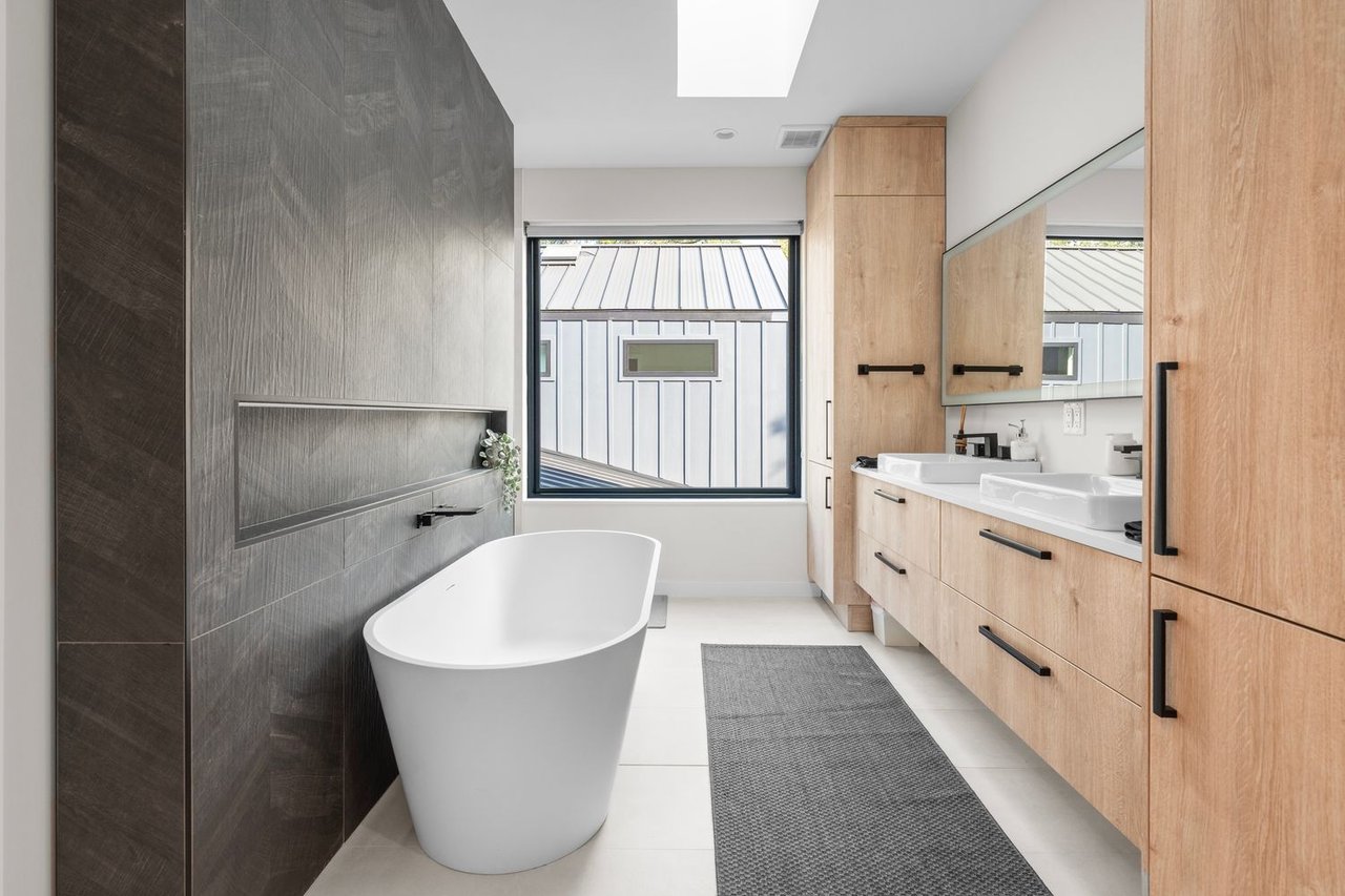 Modern bathroom with a freestanding tub, dark tiled wall, and light wood double vanity.