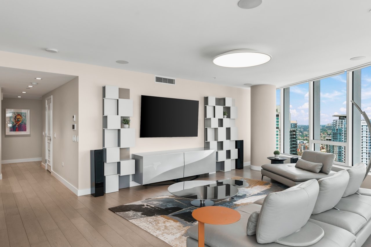 Furnished living room with a white sectional and floor-to-ceiling windows overlooking the city.