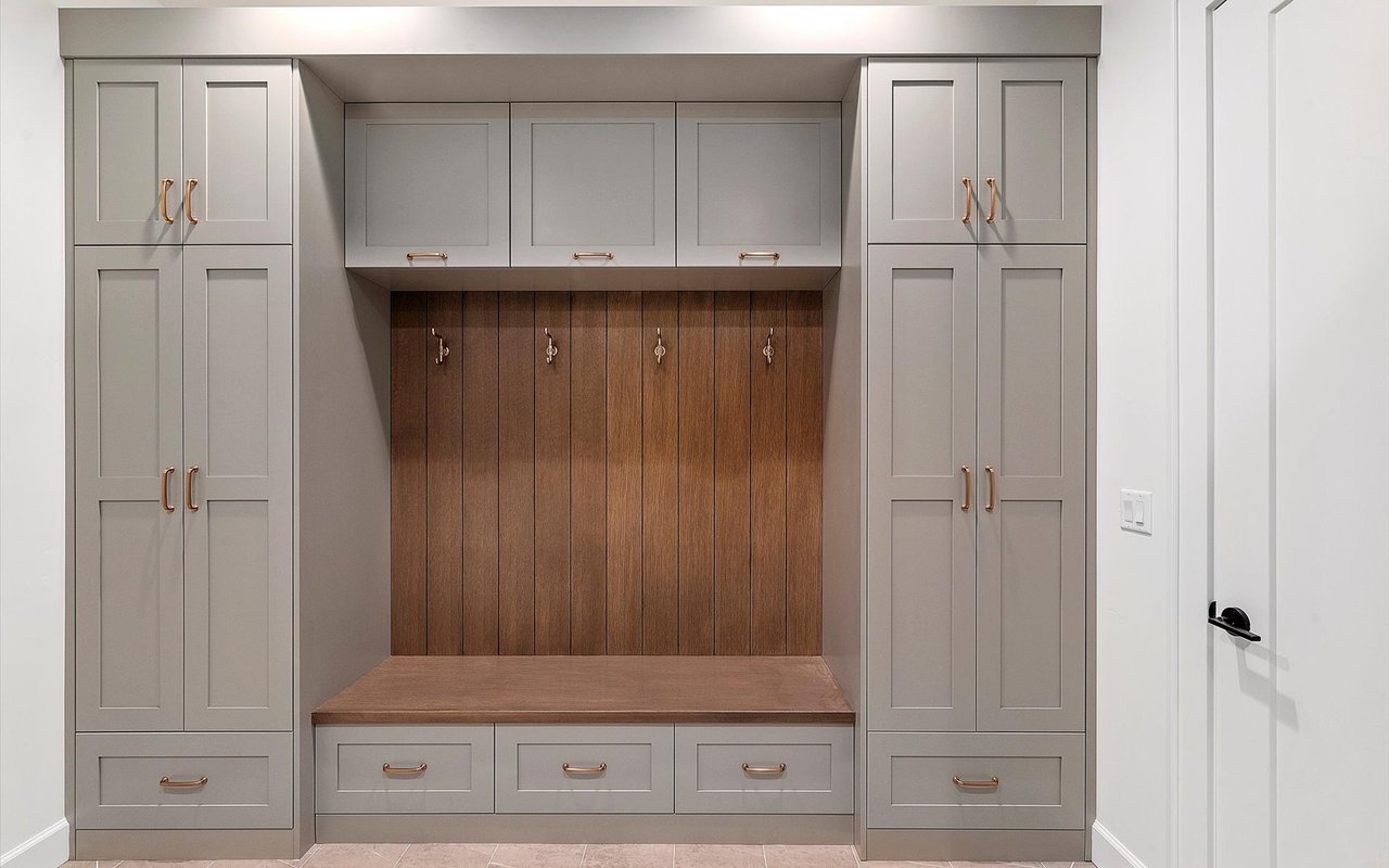 Mudroom/drop zone with gray painted cabinets, medium-wood shiplap and bench, and brass hardware