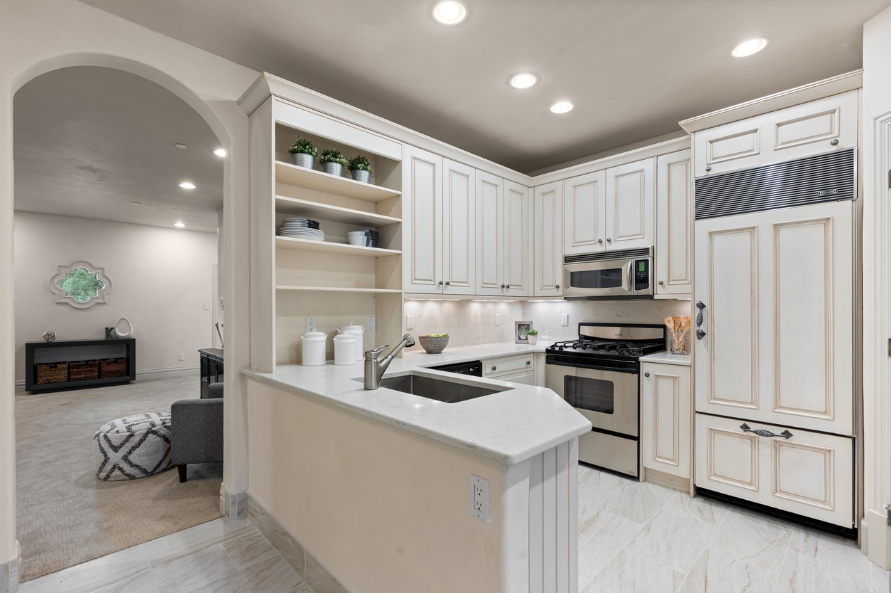 Kitchen with white cabinetry, a marble-look peninsula, stainless steel appliances, and an arched opening to a sitting area.