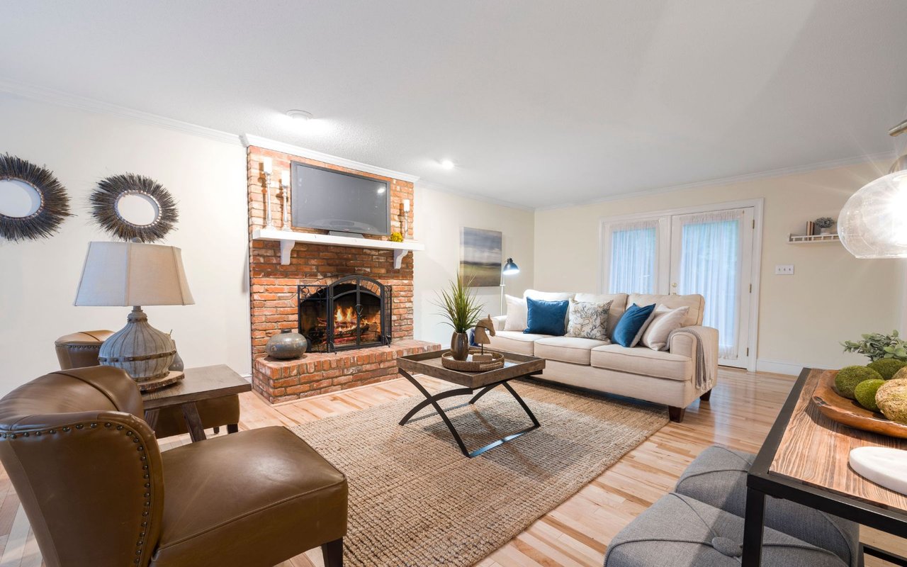Furnished living room with a brick fireplace, cream sofa, and brown leather chairs.
