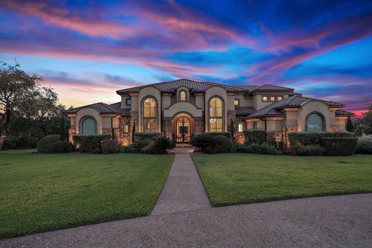 Twilight front elevation of the stone and stucco home with a tile roof at 25715 Cliff Circle, Lakecliff on Lake Travis, Spicewood, Texas.