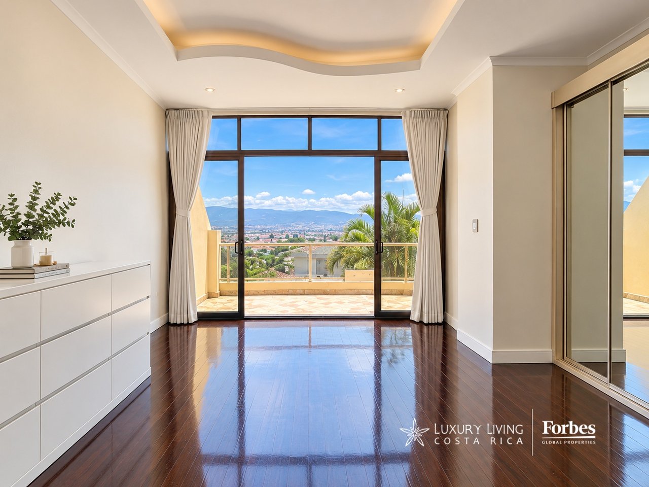 Penthouse interior with polished hardwood floors, sliding glass doors, and a terrace overlooking the city and mountains.
