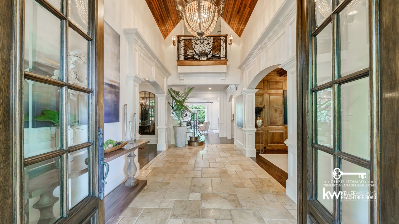 Elegant foyer with a vaulted wood ceiling, chandelier, stone floor, and wrought-iron balcony railing.
